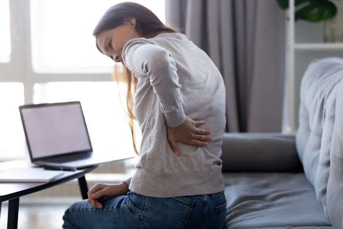 Woman holding her lower back while working at a laptop